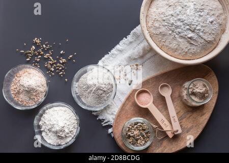 ingredients to bake homemade sourdough: rye, wholegrain, plain wheat flour, seeds, starter arranged on grey table
