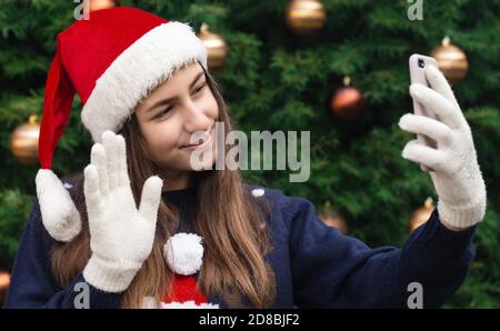 Christmas online greetings. girl in santa claus hat talks and using mobile smartphone for video call friends and parents. Christmas during coronavirus Stock Photo