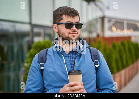 Young man drinks coffee from paper cup outside. Stock Photo