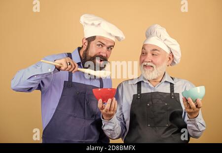 Eat concept. Mature bearded men professional restaurant cooks. Delicious recipe. Kitchen team prepare food. Family tradition. Chef men cooking. Culinary dynasty. Teaching culinary. Culinary book. Stock Photo