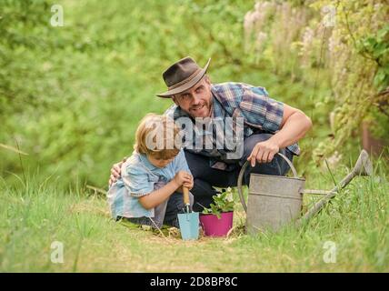 Boy and father in nature with watering can. Gardening tools. Planting flowers. Dad teaching little son care plants. Little helper in garden. Make planet greener. Growing plants. Take care of plants. Stock Photo
