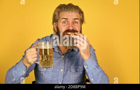 Consume alcohol. Enjoy your meal. Beer and food. Dinner at pub. Hungry man drink beer and eat snacks. Bar restaurant. Cheerful man bearded hipster drinking beer. Friday party concept. Good appetite. Stock Photo