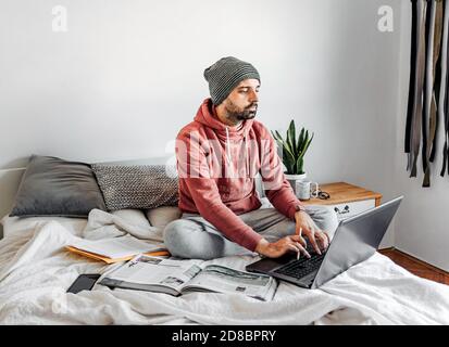 Young man sitting on his bed and typing on his laptop Stock Photo
