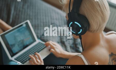 Young caucasian blond woman with headset playing game on the laptop in her bedroom. High quality photo Stock Photo