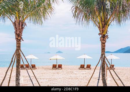 Beach chairs on the sandy beach in palm trees frame. Minimal style seascape. Photo with blur in motion and soft focus. Vietnam, Nha Trang. Stock Photo