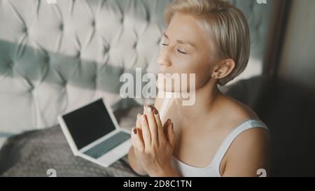 Young blonde woman praying or meditating in her bedroom. Online meditation session. High quality photo Stock Photo