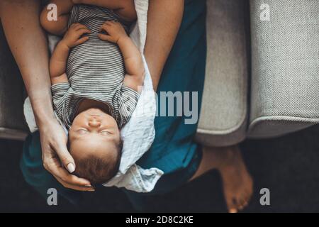 Upper view photo of a caucasian mother holding her newborn girl on her legs sleeping while posing on a sofa near free space Stock Photo