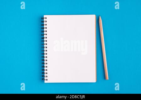 Above top overhead close up view photo of opened memory pad with blank page and wooden pencil isolated over bright color blue background with copy spa Stock Photo