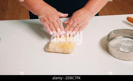 Closeup shot of hands of senior bakery kneading dough. Retired elderly baker with bonete mixing ingredients with sifted wheat flour forming on a floured surface for baking traditional cake, bread Stock Photo