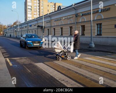 Moscow. Russia. October 28, 2020. One woman with a baby carriage crosses the road at a pedestrian crossing. The car has stopped and gives way to a Stock Photo