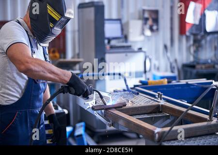 Mechanic in protective helmet welding metal car parts in garage Stock Photo