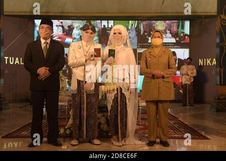 Two brides wearing traditional Javanese clothes and masks are getting married during a wedding ceremony at the Ambarukmo Hotel Yogyakarta. At the same time, 9 other brides are also having weddings in several different regions. The ceremonies are displayed on the screen and witnessed by invited guests virtually from the Yogyakarta Ambarukmo Hotel. The bride and groom must implement the health protocol, washing hands, wearing masks and keeping a distance.  Indonesia. Stock Photo