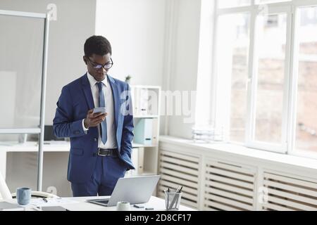 Young African businessman typing a message on mobile phone standing near his workplace at modern office Stock Photo