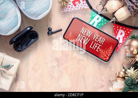 New Year New Life resolutions fitness healthy goals concept. New Year New Life text on mobile phone on table with sport shoes, wireless earphone,  and Stock Photo