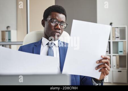 African businessman in eyeglasses holding papers in his hands examining documents while working at office Stock Photo