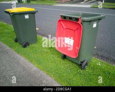 AUCKLAND, NEW ZEALAND - Oct 11, 2019: View of two rubbish containers with red and yellow lids on green grass Stock Photo