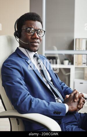 Portrait of African young businessman in formalwear wearing headphones sitting on chair and looking at camera Stock Photo