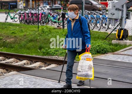 Old man with mask with walking stick crossing the train tracks in Prague Stock Photo