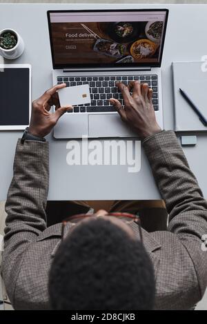 High angle view of African businessman holding credit card and paying online for food using laptop Stock Photo