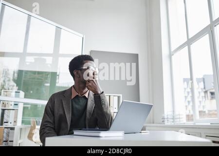 African businessman sitting at the table in front of laptop and thinking about new ideas at office Stock Photo