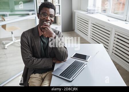Portrait of African successful manager smiling at camera while working at the table on laptop Stock Photo