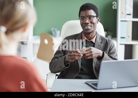 African young businessman smiling and talking to the woman sitting at the table during meeting Stock Photo