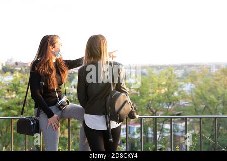 Two girls looking at the city from a viewpoint. They are wearing face masks. Space for text. Stock Photo