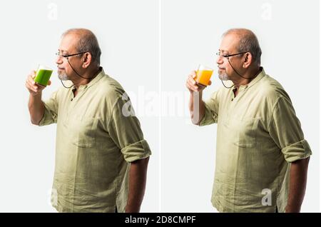 Indian asian senior or old man drinking fresh orange juice in a glass while standing against white background Stock Photo