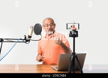 Confident Indian old man speaking in recording mic with filter while recording a video blog for his subscribers, looking at camera Stock Photo