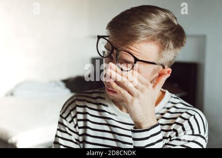 Tired exhausted man taking off glasses, feeling eye strain after work. man suffering from dry eye syndrome, fatigue rubbing eyes migraine headache aft Stock Photo