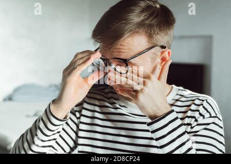 Tired man taking off glasses rubbing dry irritated eyes to relieve pain feeling discomfort suffers eye strain, poor blurry vision isolated on white ba Stock Photo