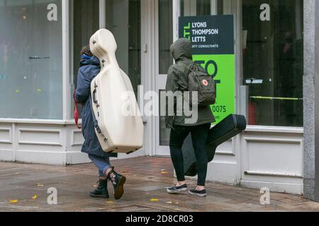 Preston, Lancashire.  Uk Weather. 29th October 2020. Musicians pcarrying instruments in case in the city centre on a wet rainy day with heavy downpours, and merging showers.  Preston retail sector has been heavily affected by Covid 19 regulations with several businesses closing in the high street.   Credit; MediaWorldImages/AlamyLiveNews Stock Photo