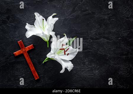 Funeral lily flowers with cross on dark stone background. Mourning symbols Stock Photo