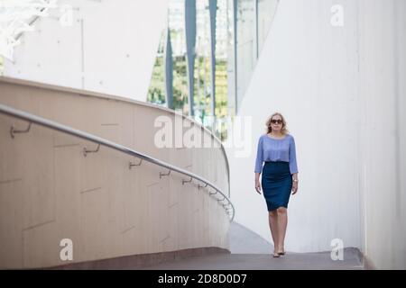 Blonde woman in a skirt is walking down the street in summer Stock Photo