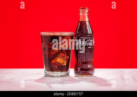 London, United Kingdom - October 29 2020:  Ice cold glass bottle of Coke sits next to a full glass of Coke with condensation and ice cubes Stock Photo