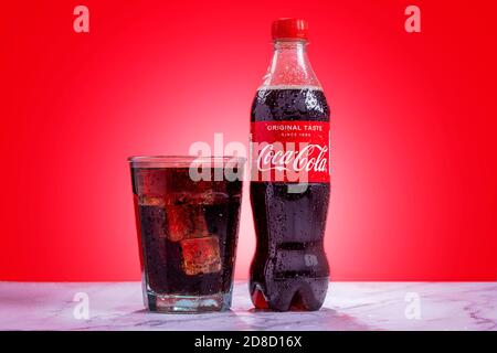 London, United Kingdom - October 29 2020:  Ice cold plastic bottle of Coke sits next to a full glass of Coke with condensation and ice cubes Stock Photo