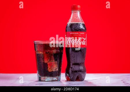 London, United Kingdom - October 29 2020:  Ice cold plastic bottle of Coke sits next to a full glass of Coke with condensation and ice cubes Stock Photo