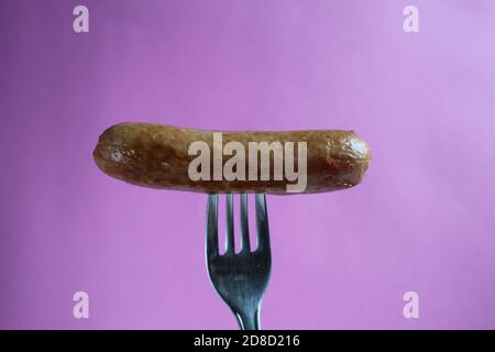 a sausage a fried sausage is pinned on a fork on a purple fuchsia background copy space Stock Photo