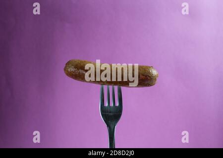 a sausage a fried sausage is pinned on a fork on a purple fuchsia background copy space Stock Photo