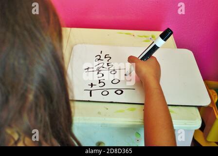 Second grade girl learning how to carry the one on a whiteboard while distance learning not common core math Stock Photo