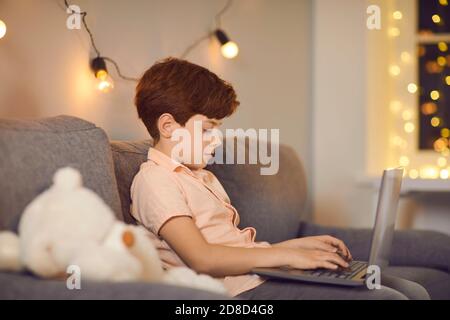 Boy sitting on sofa with laptop and typing message during online communication Stock Photo