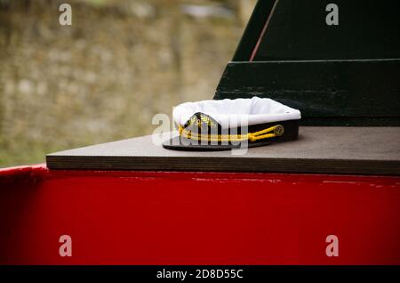 close up of black and white sailors hat with brass anchor buttons,  on the end of a red and black canal boat outside Stock Photo