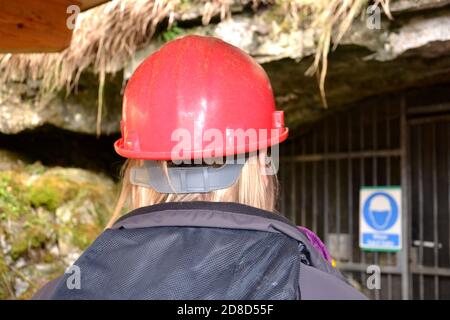 close up of woman wearing a protective red helmet and grey jacket at entrance of a cave Stock Photo