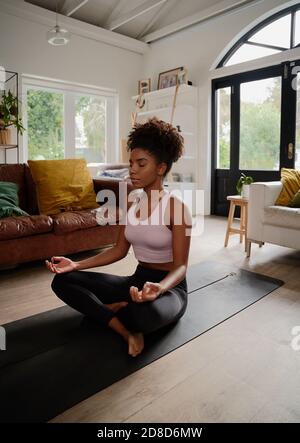 African young woman in lotus position practising meditation and breathing exercise at home Stock Photo