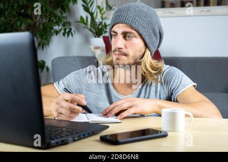 Handsome young caucasian man using computer working at home and learning online and writing notes Stock Photo