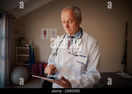 Senior male medical professional wearing labcoat and stethoscope using digital tablet Stock Photo