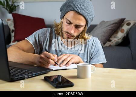 Handsome young caucasian man using computer working at home and learning online and writing notes Stock Photo