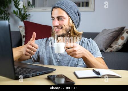 Handsome young caucasian man using computer working at home and talking with mobile feeling happy with smile showing teeth with thumbs up Stock Photo