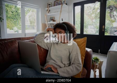 Young black student enjoying lockdown vacation by watching video on laptop with headphones at home Stock Photo