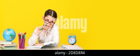 The schoolgirl sits at the desk and thinks about the decision of the task on yellow background. Back to school. The new school year. Child education c Stock Photo
